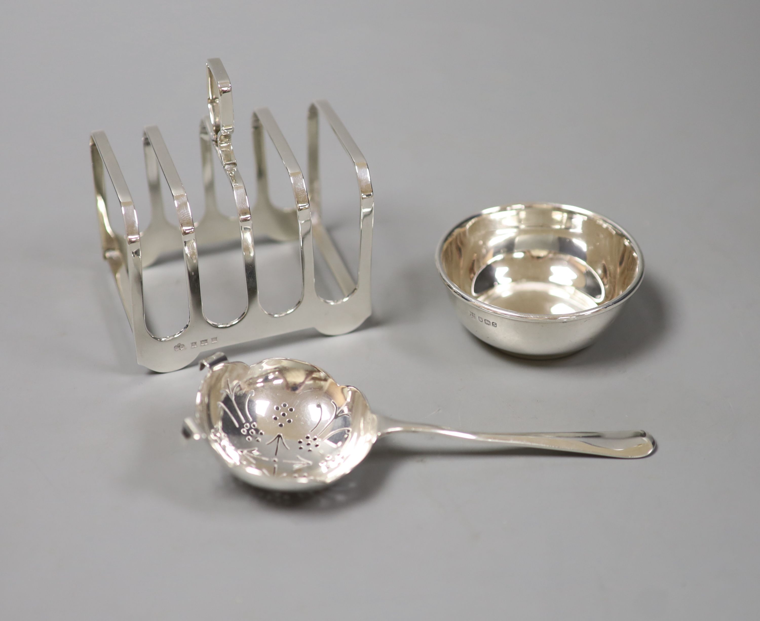 A silver four-division toast rack, a tea strainer and a drip tray,